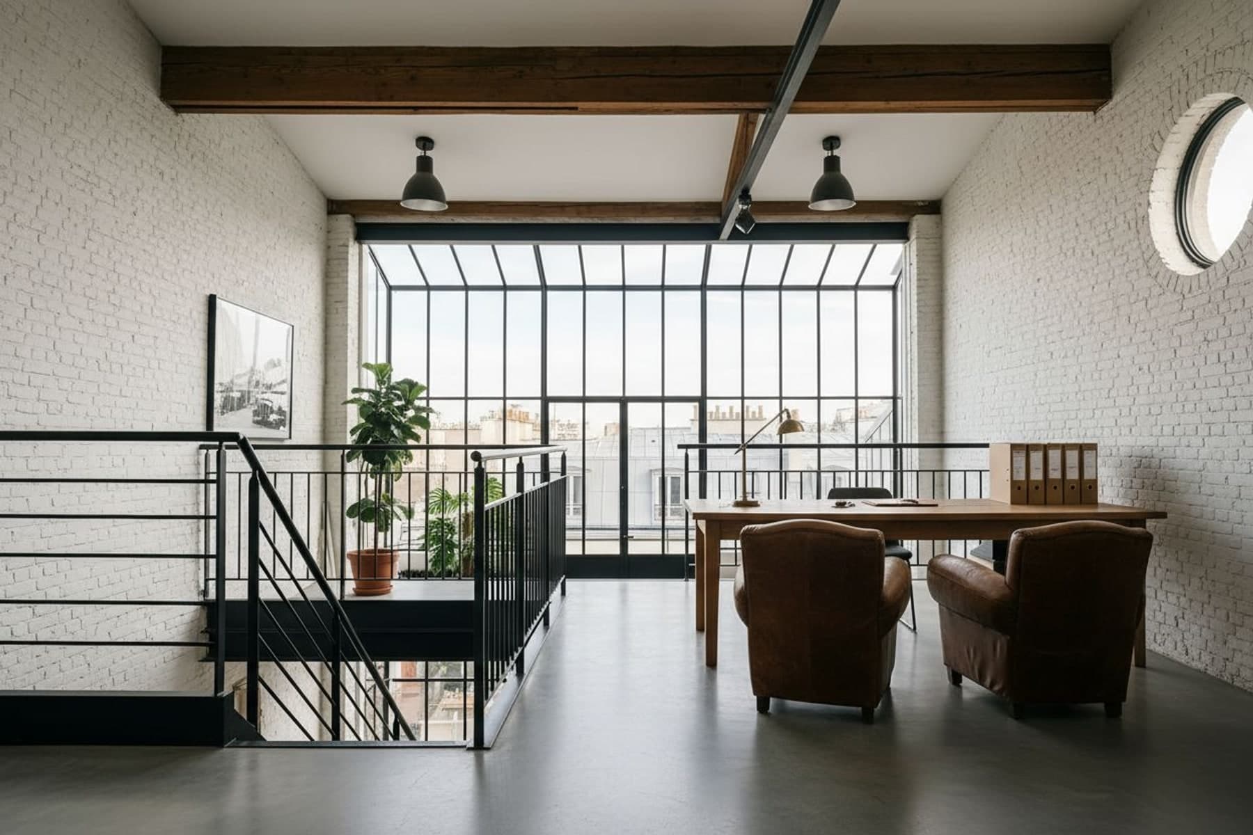 La mezzanine de l'atelier : bureau en chêne, lampe en laiton, deux fauteuils club et la verrière sur les toits